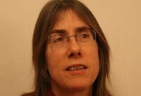 Helene Bouchiat mit offenem Haar und rotem Rollkragenpullover, neutraler Ausdruck.